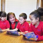Suzanne Schecdt, Principal of St. Catherine’s School in Denver, reads with Kindergarten students (l-r) Sofia Villalobos-Garcia, Noah Gillespie and Darian Lewis. She has worked as a teacher and principal for 45 years.